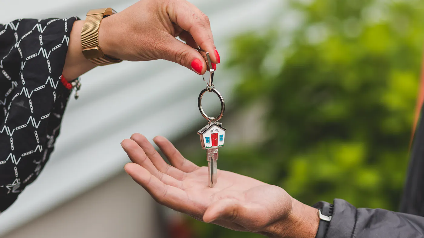 A hand handing over a key with a house keychain at a Texas title company closing